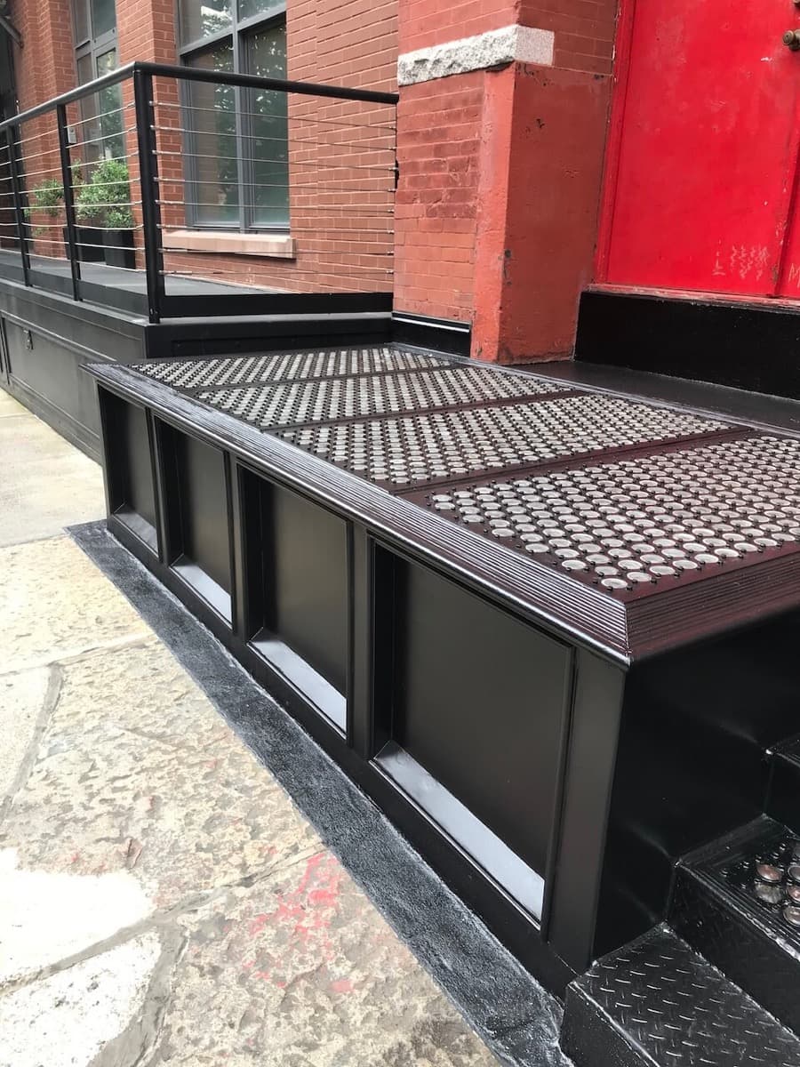 Restored black cast iron vault light platform on a SoHo sidewalk, with a red brick wall behind