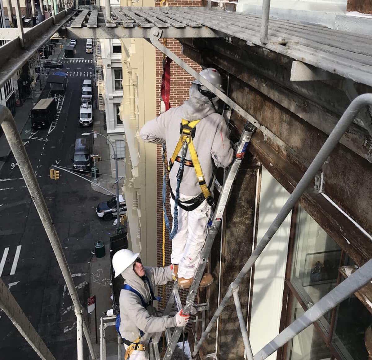 Painter in a harness on a ladder high above a SoHo street, working on a building exterior